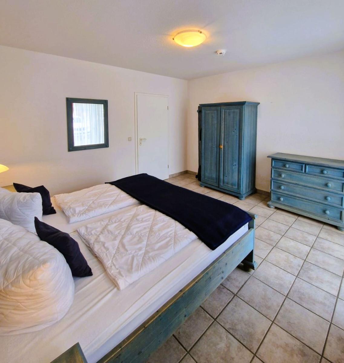 Schlafzimmer mit Bett, Kleiderschrank und Schrank. Fliesenboden und Wandspiegel.
