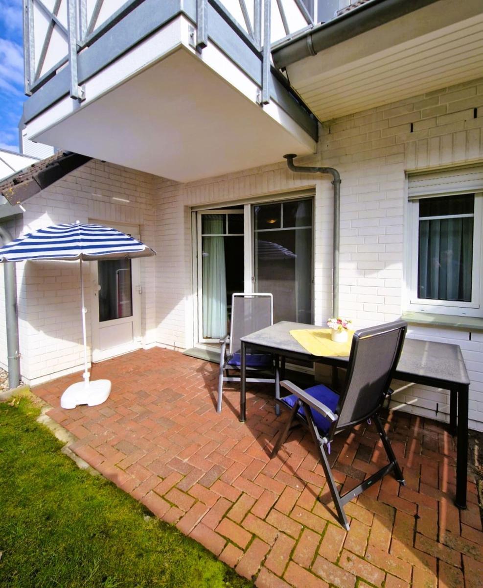 Terrasse mit Tisch, Stühlen und Sonnenschirm. Hintergrund: Haus mit Fenstern und Balkon.
