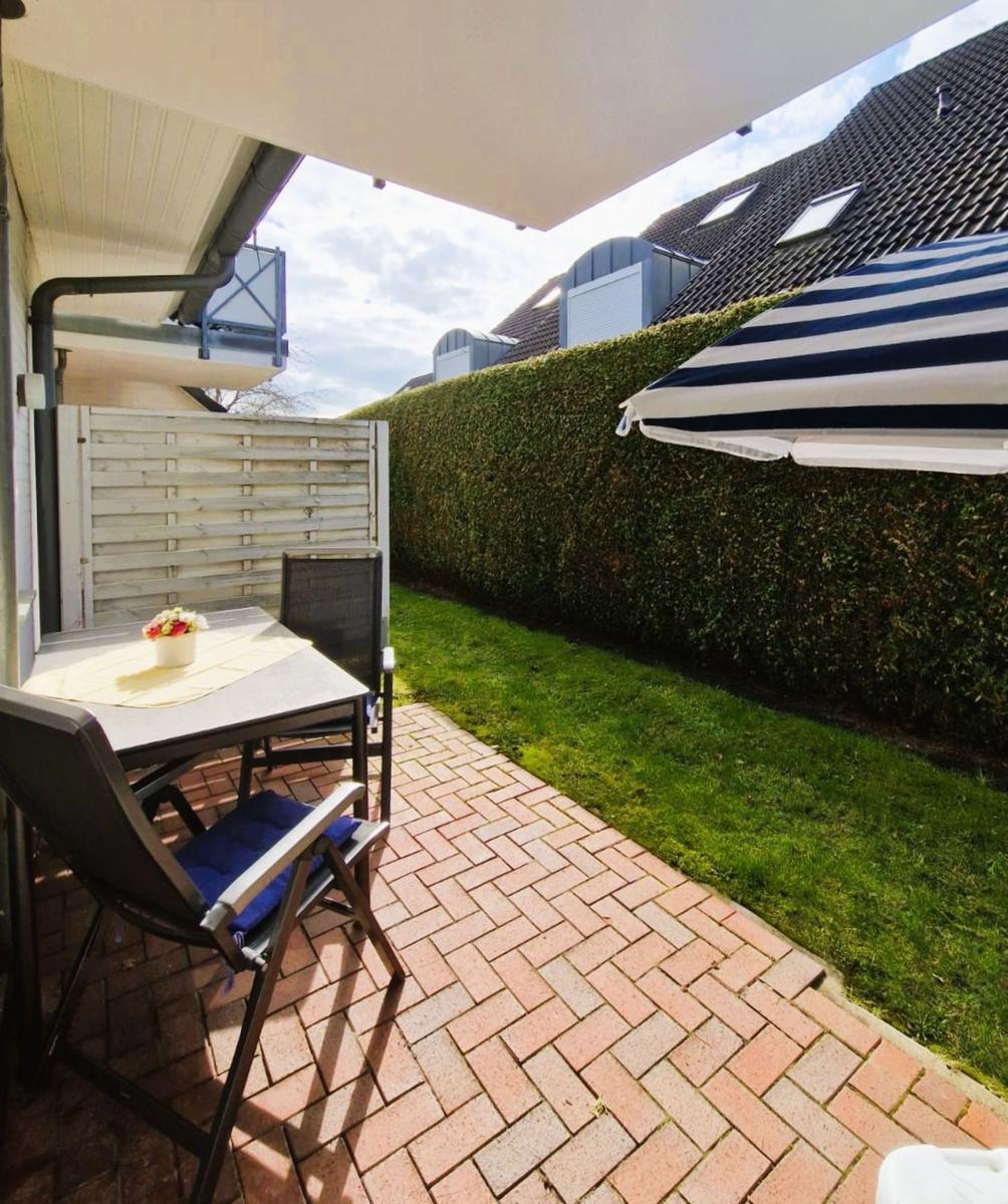 Terrasse mit Tisch, Stühlen und Sonnenschutz. Rasenfläche und Hecke im Hintergrund.