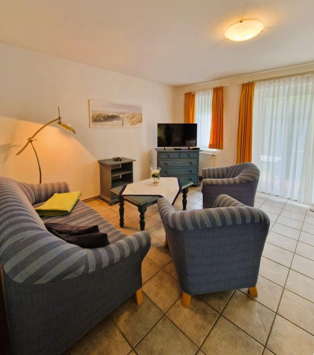 Wohnzimmer mit Sofa, zwei Sesseln, TV und Fenster mit Vorhängen.