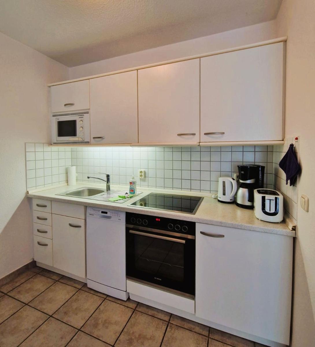 Küche mit weißen Schränken, Spüle, Herd und Kühlschrank.