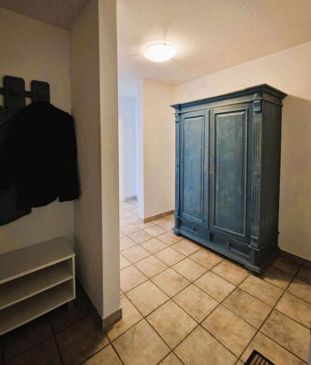 Eingangsbereich mit Kleiderständer und blauem Schrank auf Fliesenboden.