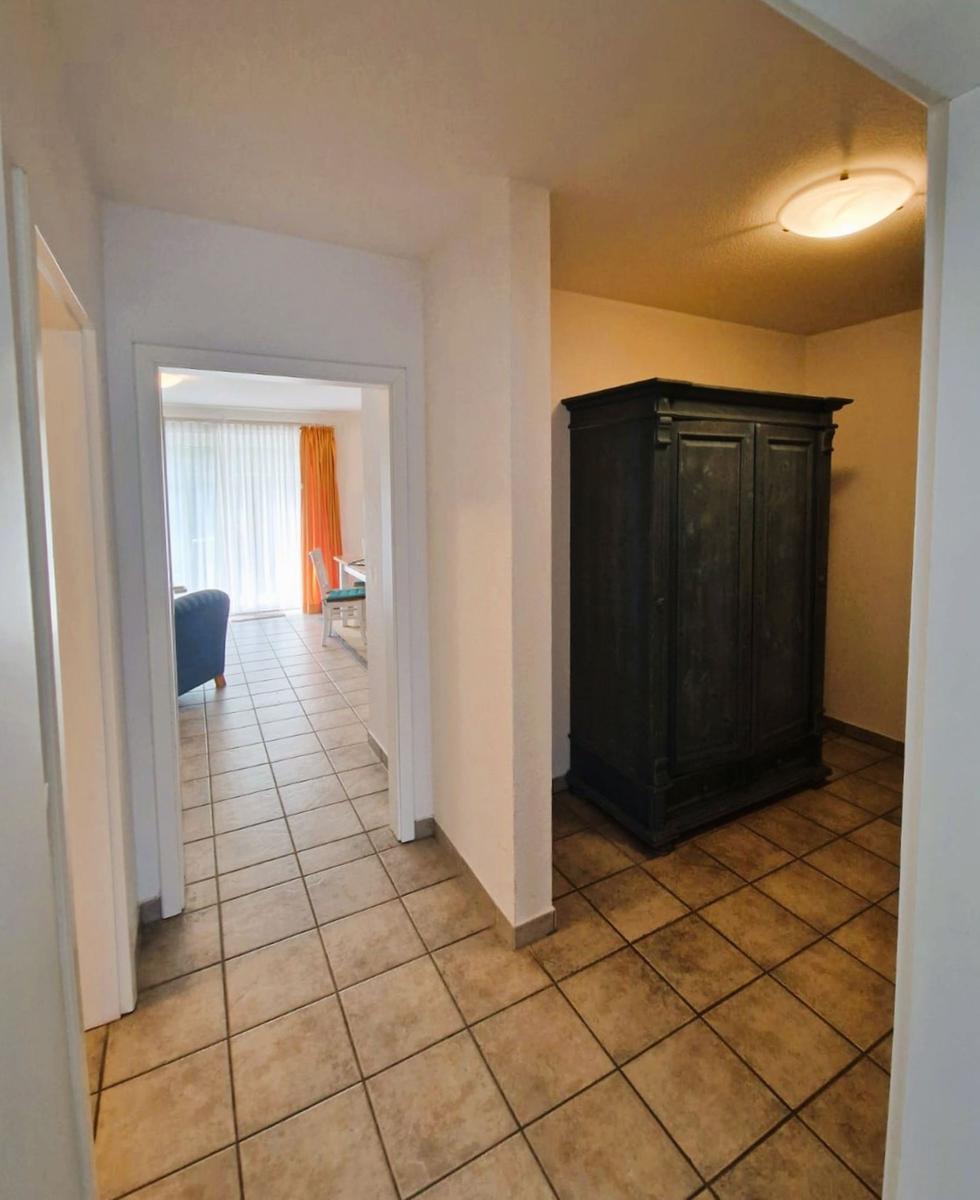 Flur mit dunklem Schrank und Blick in Wohnbereich mit orangefarbener Gardine.