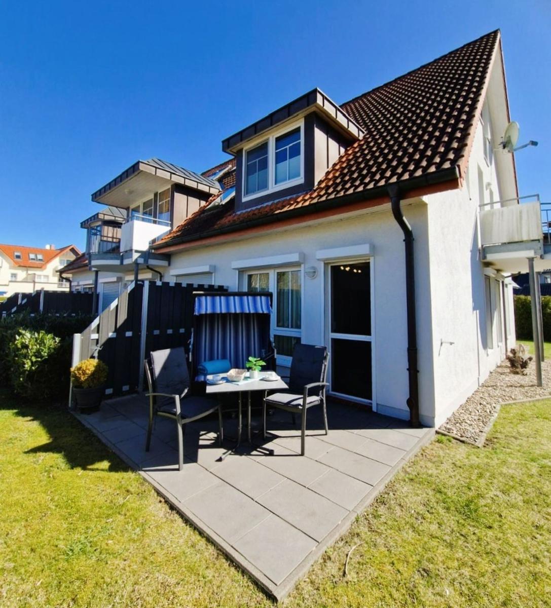 Wohnhaus mit Terrasse, Tisch, zwei Stühlen und Sonnenschutz.