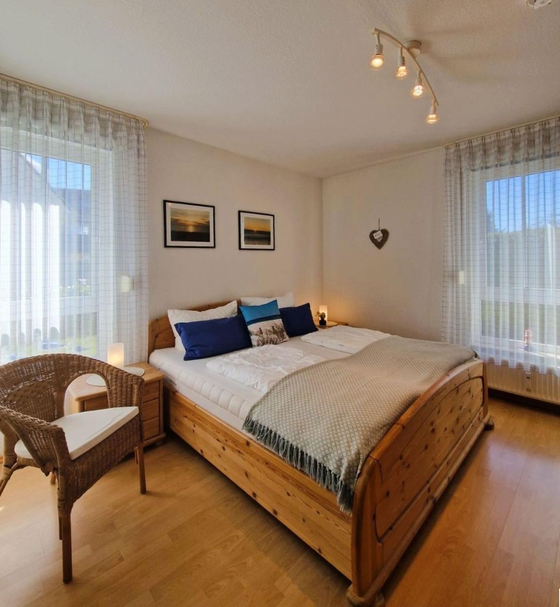 Schlafzimmer mit Holzbett, Fenstern und Stuhl