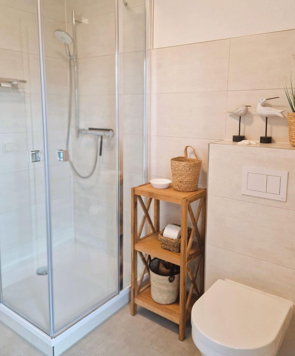 Dusche mit Glaswand, Holzregal und Toilette in einem Badezimmer.
