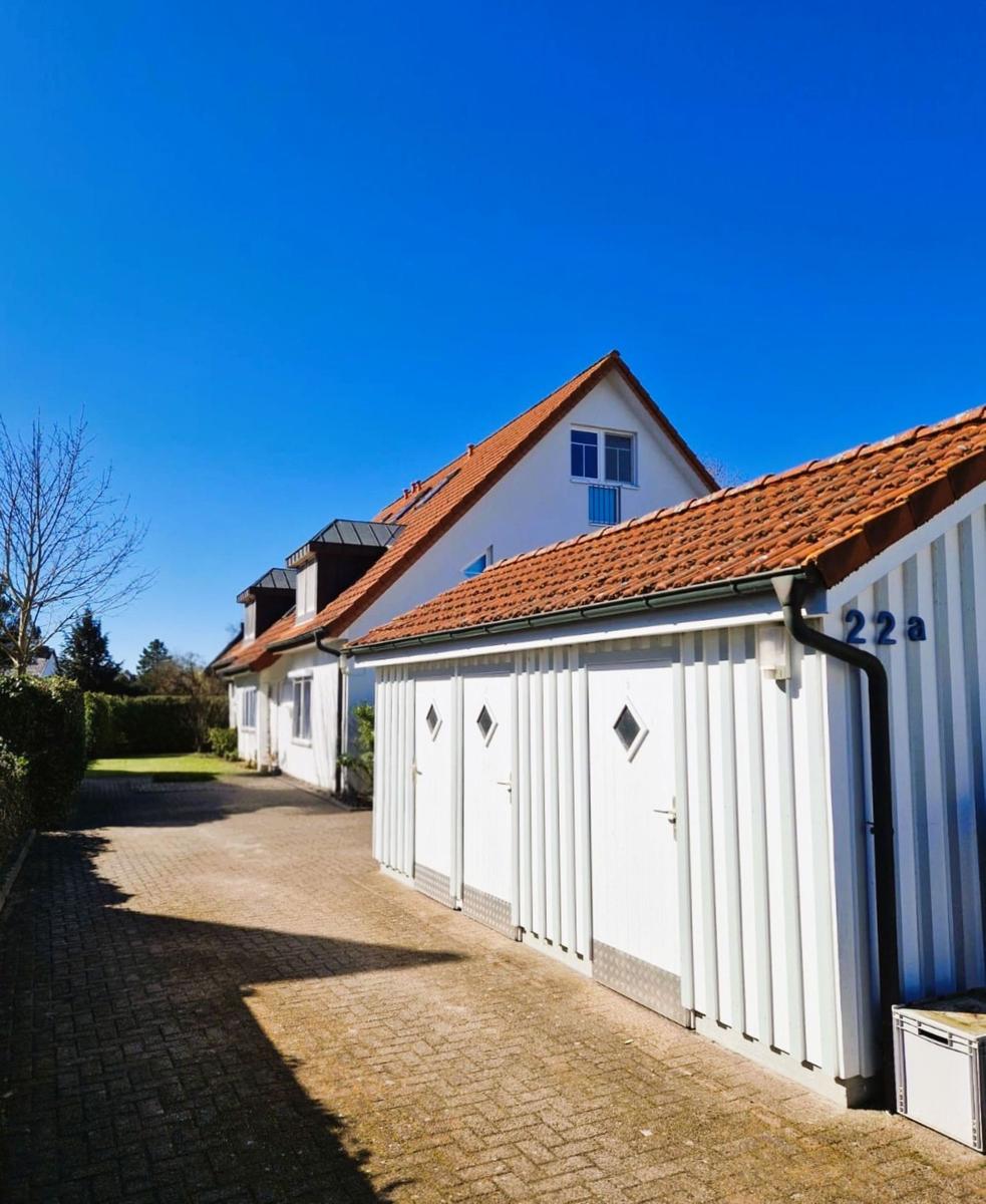Reihenhaus mit rotem Dach und weißen Garagenboxen an sonnigem Tag.