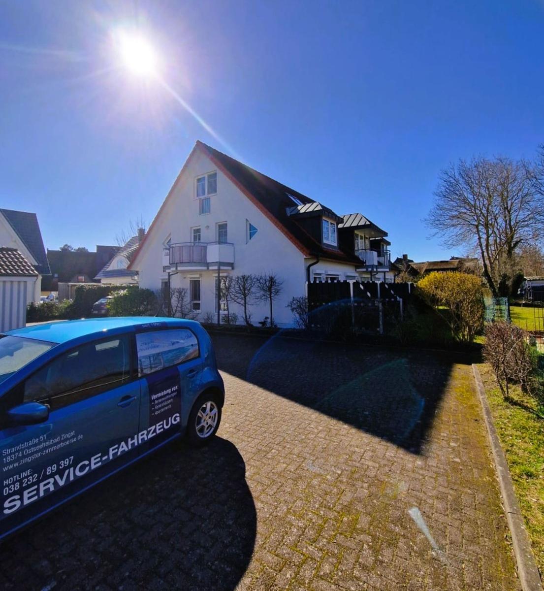 Wohnhaus mit Balkon, gepflasterter Hof und blauem Servicefahrzeug im Vordergrund.