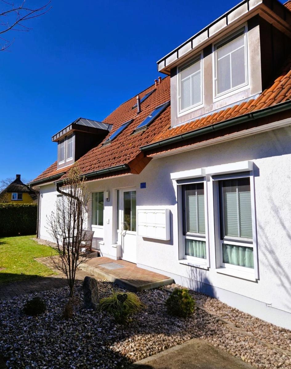 Ein Haus mit weißer Fassade, rotem Dach und Fenstern mit Jalousien.