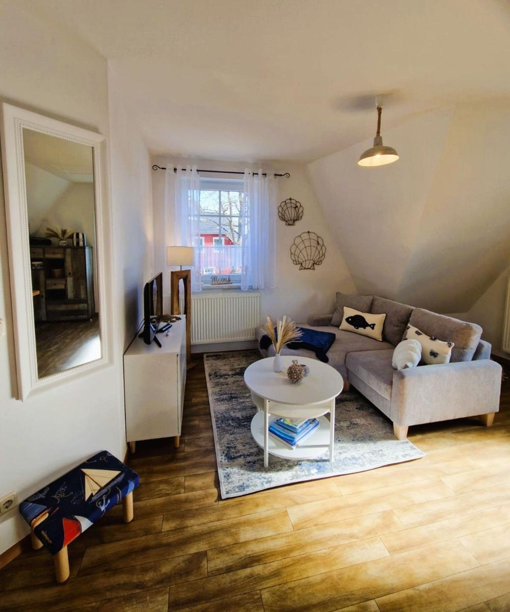 Wohnzimmer mit Sofa, runden Tisch und Holzboden. An der Wand hängen Muscheldekorationen.