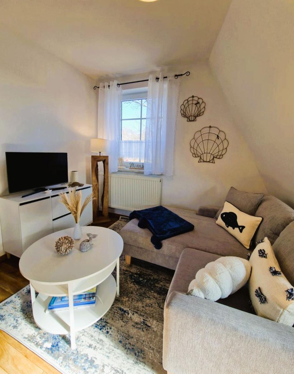 Wohnzimmer mit Sofa, runden Tisch und Fenster mit weißen Vorhängen.