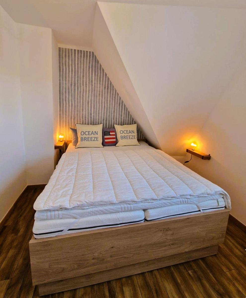 Schlafzimmer mit Doppelbett, Holzboden und schrägen Wänden. Zwei Nachttische mit Lampen.