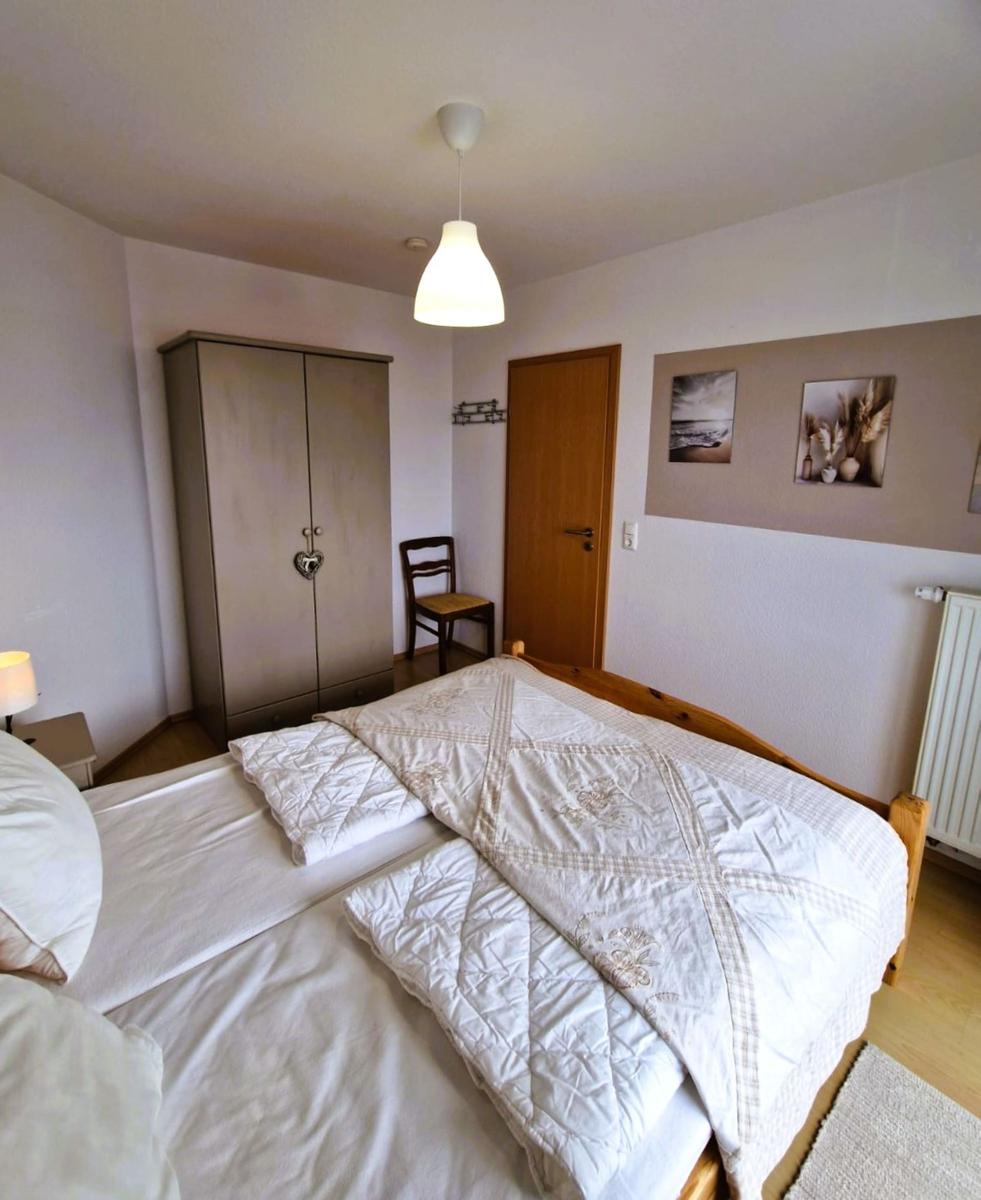 Schlafzimmer mit Bett, Kleiderschrank, Stuhl und Wandbildern.