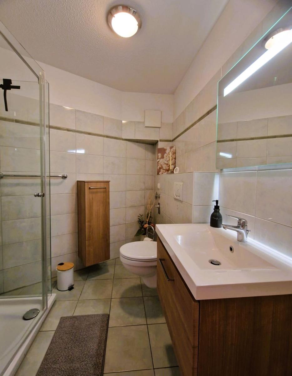 Badezimmer mit Dusche, Waschbecken und Toilette. Holzfronten und Fliesenwand.