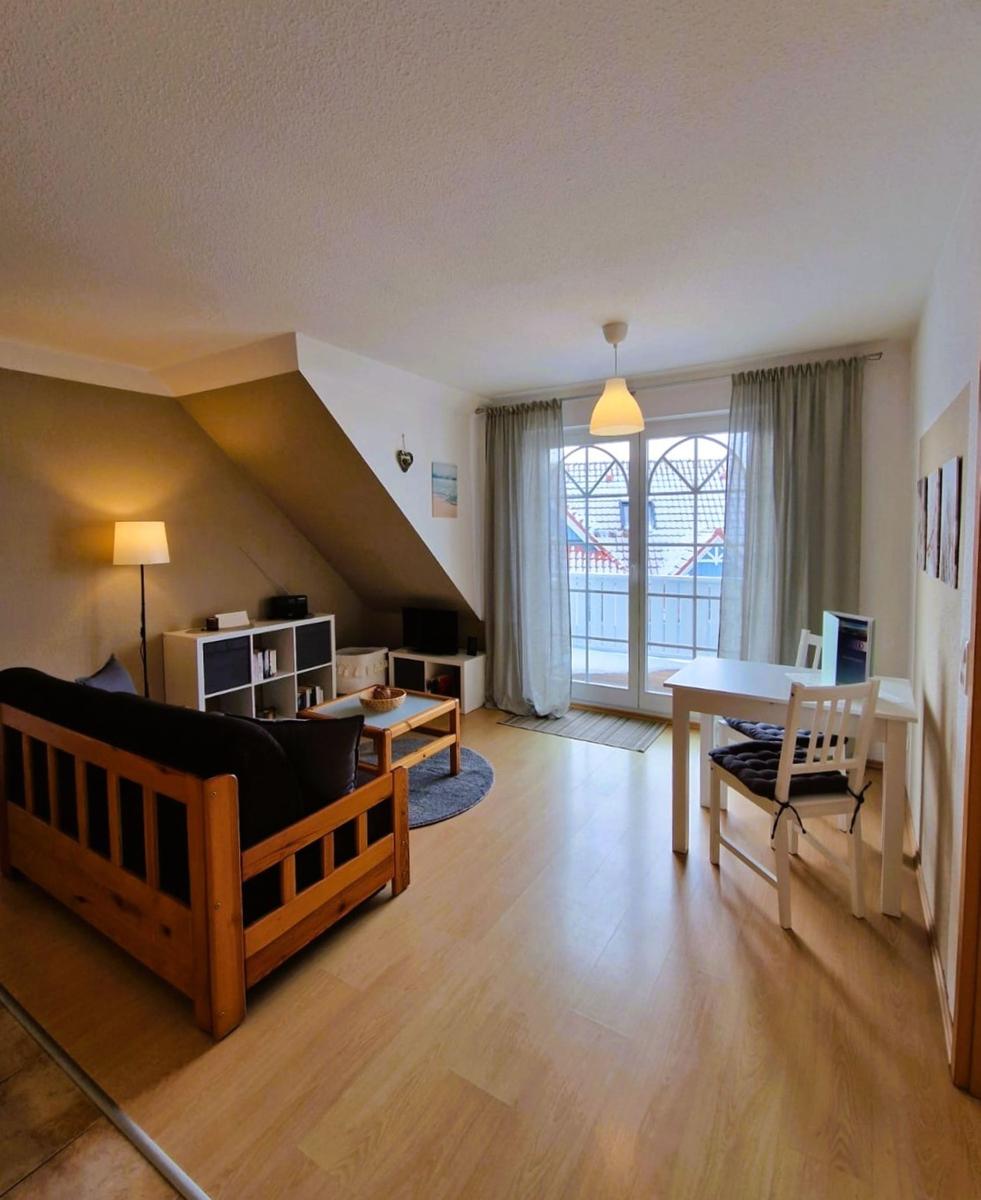 Wohn- und Essbereich mit Holzboden, Sofa, Tisch und Blick auf Balkon.