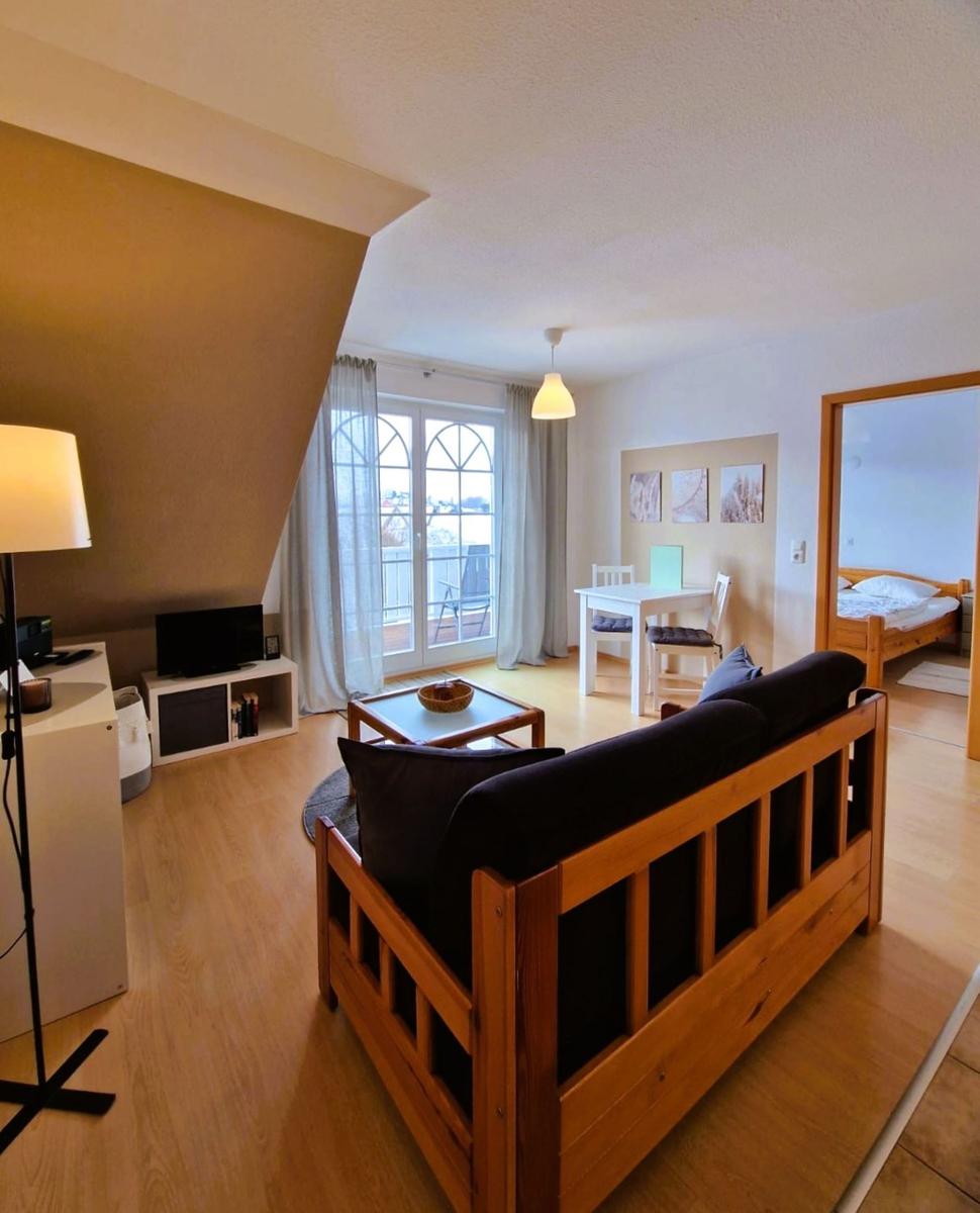 Wohnbereich mit Sofa, Essplatz und Schlafzimmer im Hintergrund.