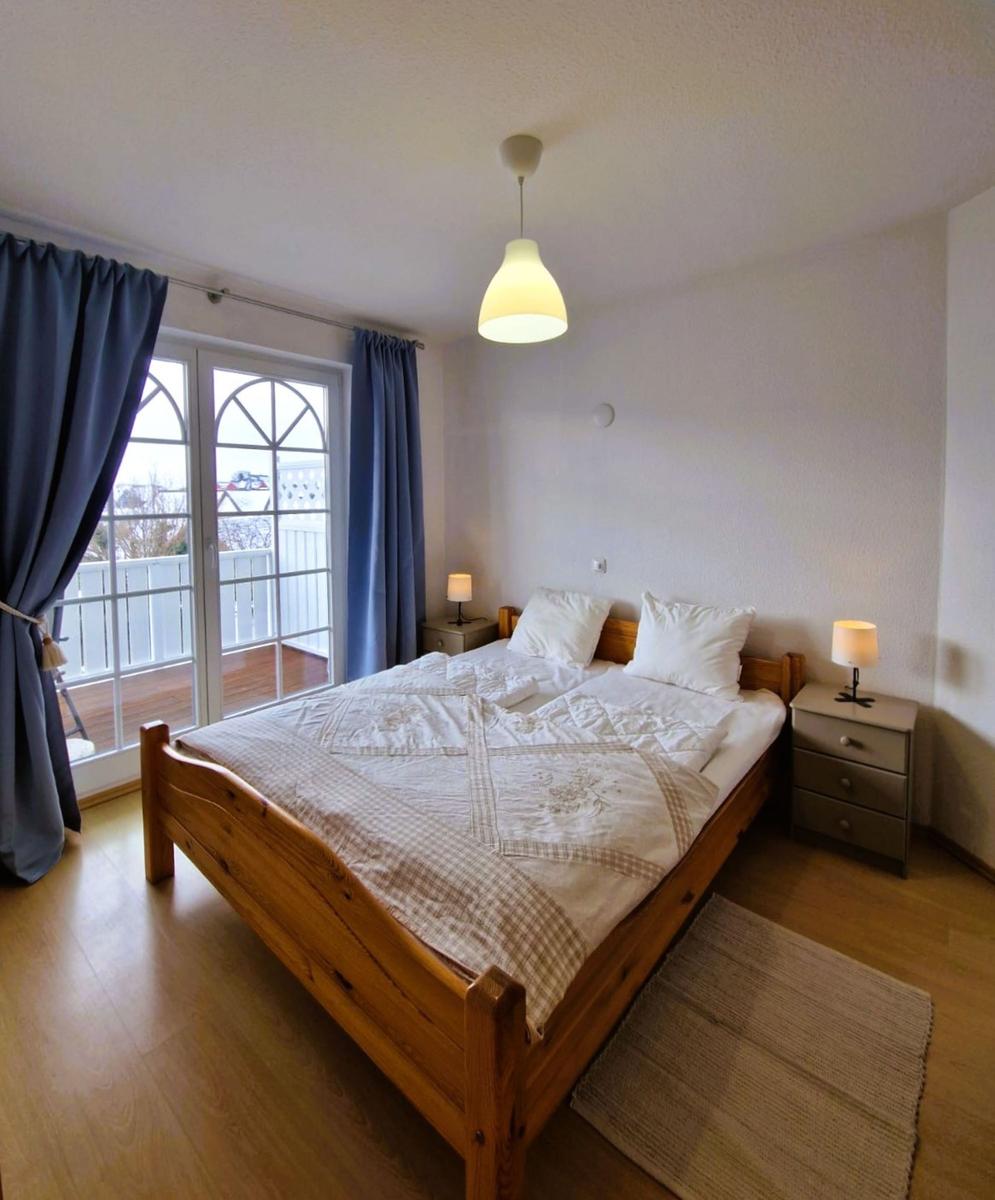 Schlafzimmer mit Holzbett, zwei Nachttischen und Balkontür.
