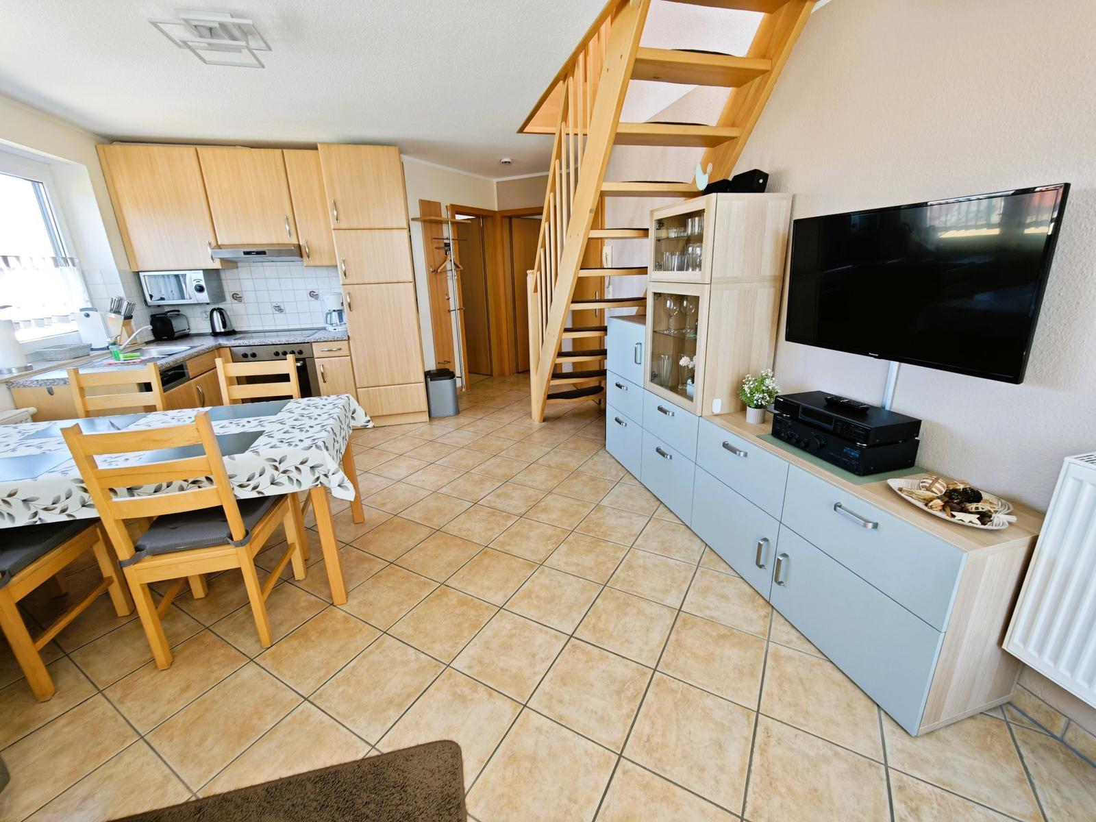 Wohnküche mit Essbereich, Holztreppe und TV-Möbel.