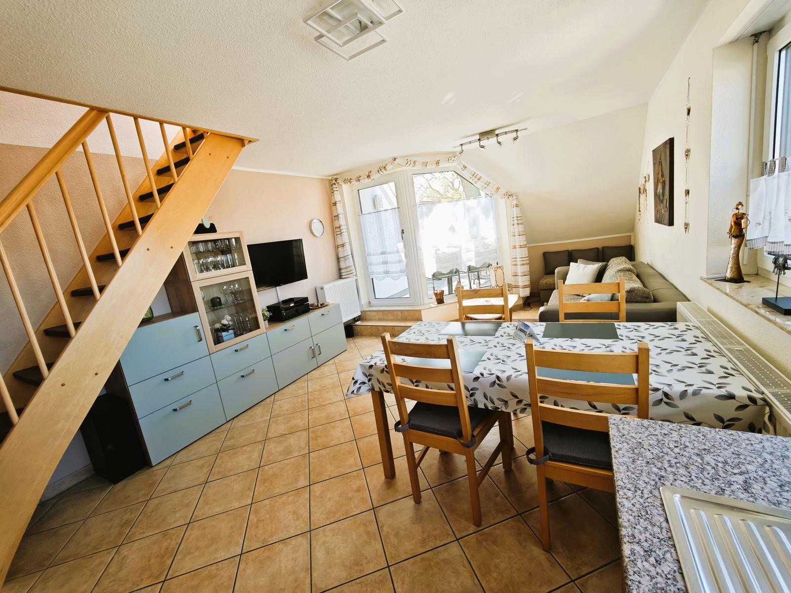 Wohn- und Essbereich mit Tisch, Stühlen, Sofa und Treppenhaus.