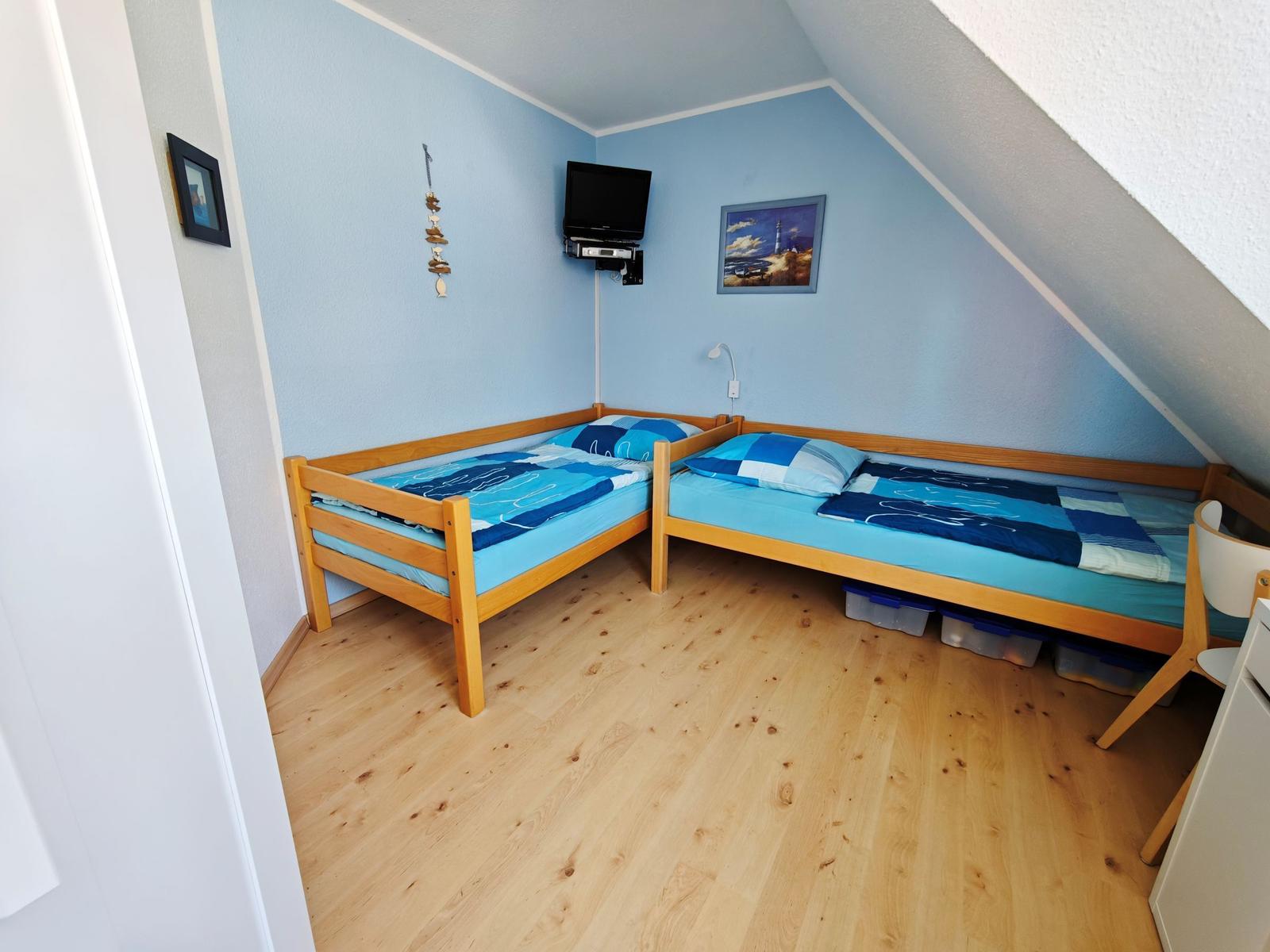 Zwei Einzelbetten mit blauer Bettwäsche, Holzboden und schräger Decke.