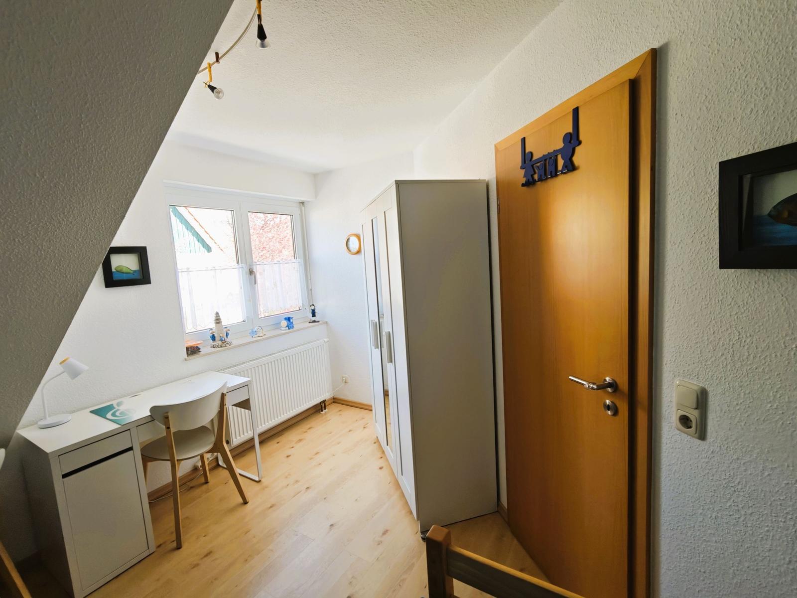 Ein Zimmer mit Schreibtisch, Fenster, Kleiderschrank und Tür mit Dekoration.