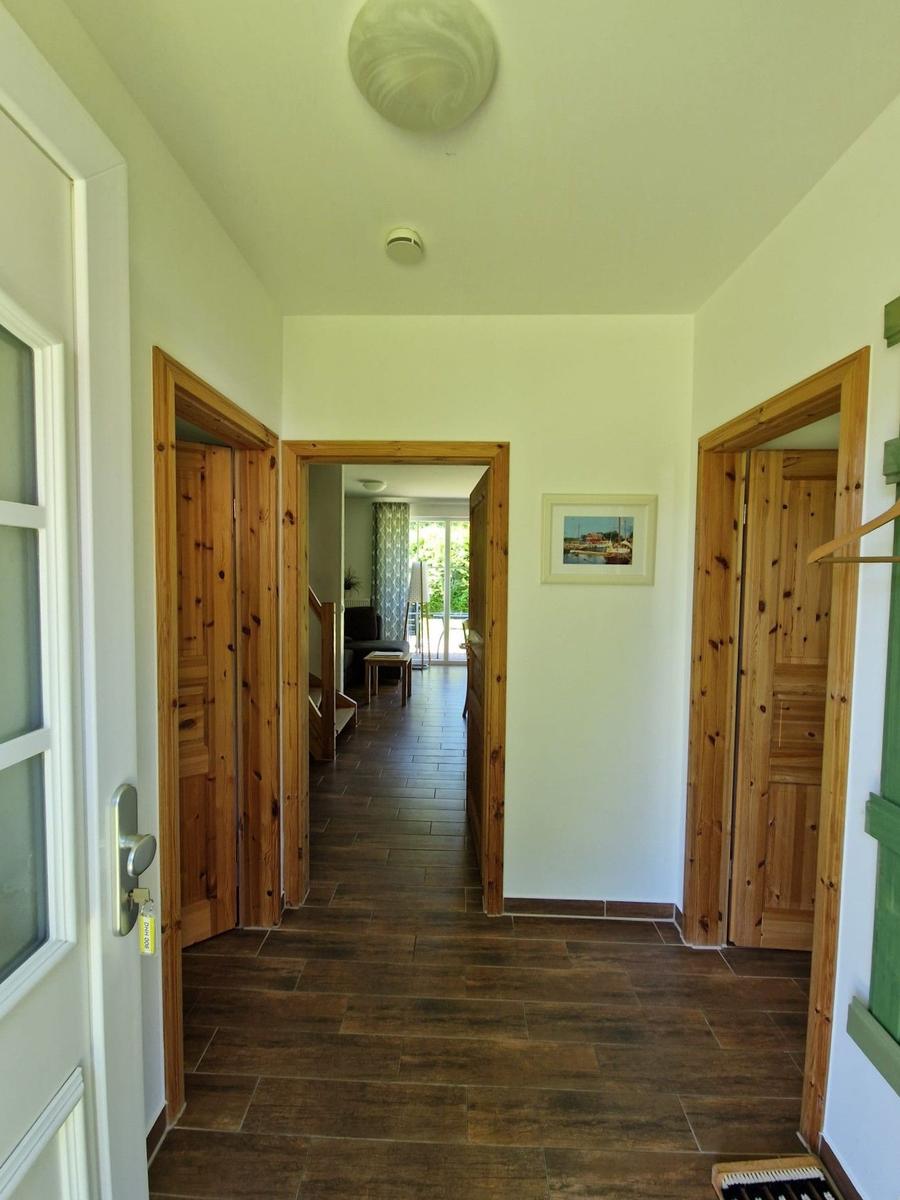 Flur mit Holztüren und dunklem Boden. Im Hintergrund ist ein Wohnbereich mit Fenster sichtbar.