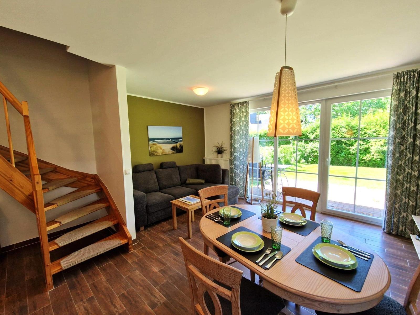 Esszimmer mit Tisch, Stühlen und Blick auf Garten. Treppenhaus und Wohnbereich sichtbar.