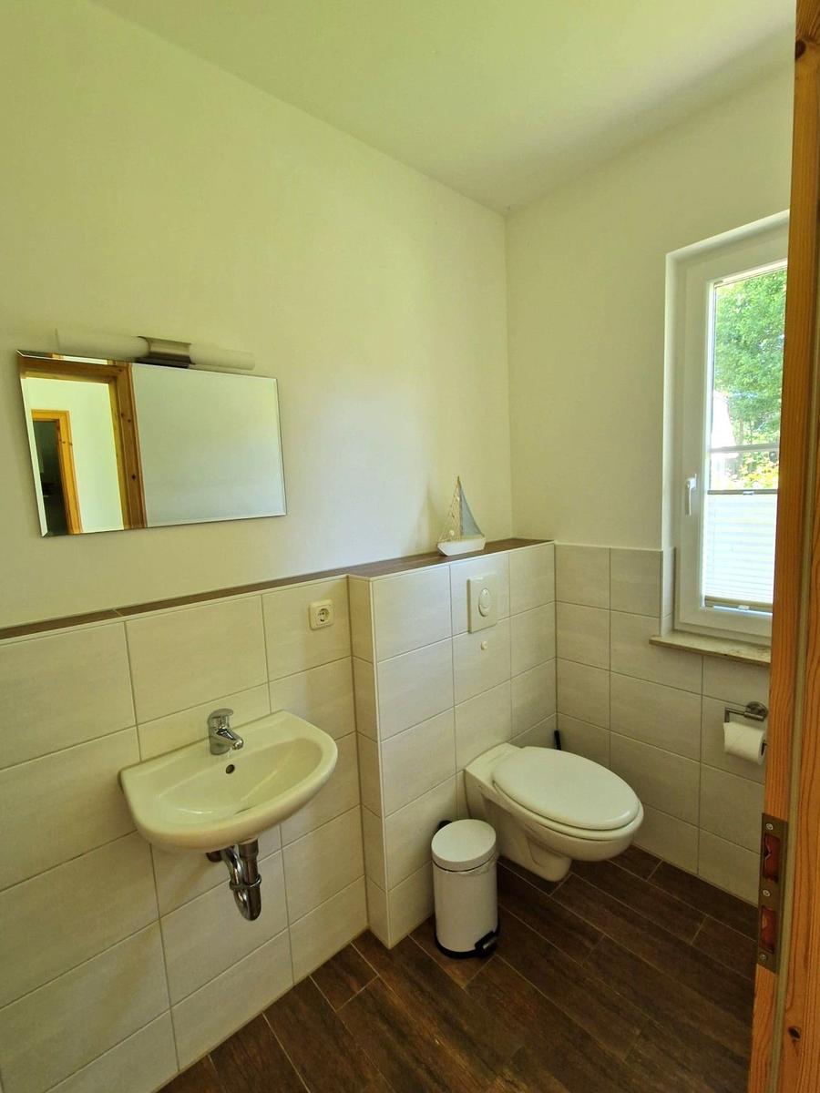 Badezimmer mit Waschbecken, Toilette und Fenster. Wandverkleidung und Holzboden.