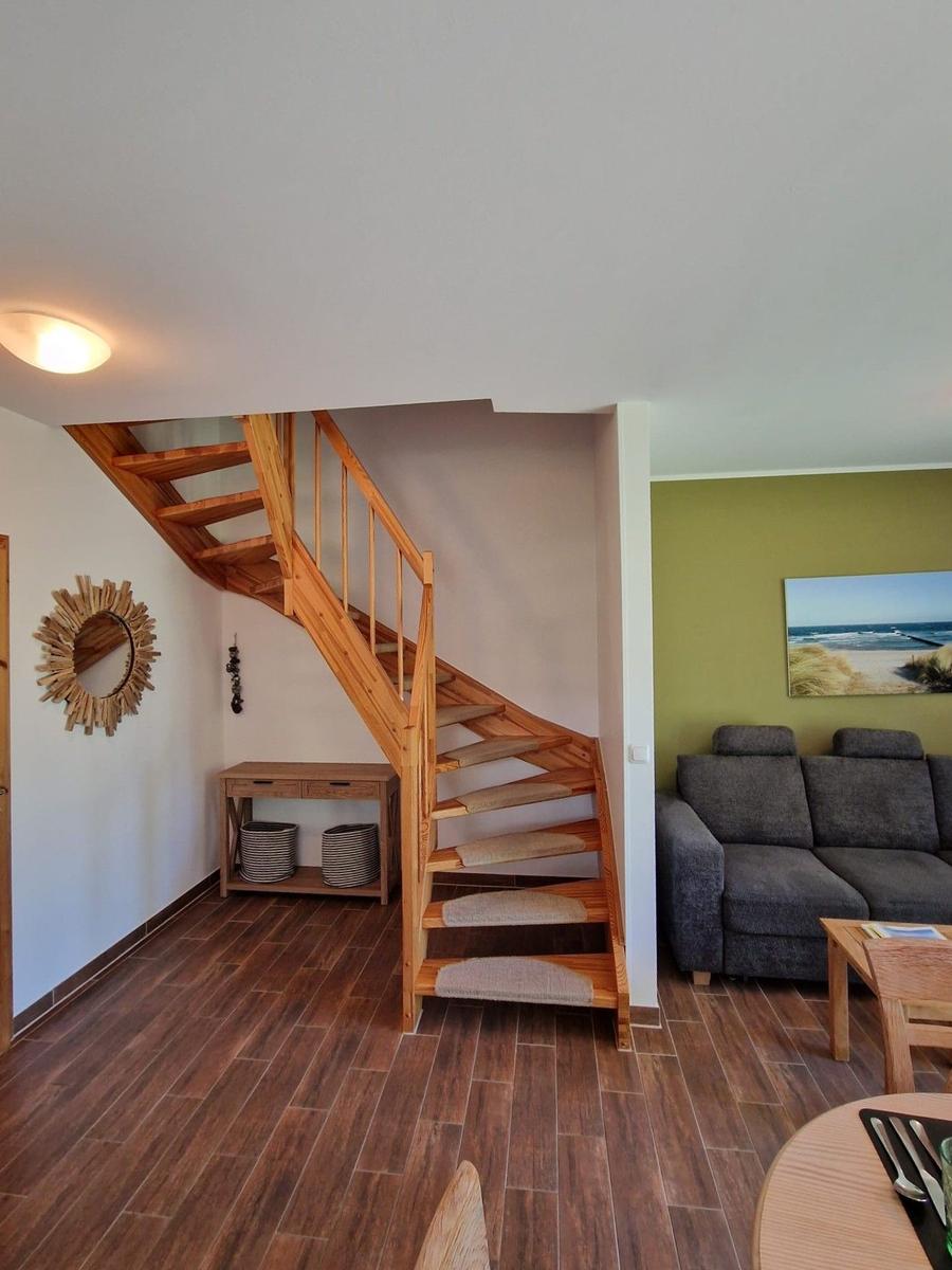 Holztreppe führt zu einer oberen Etage. Wohnbereich mit Sofa und Wandbild.