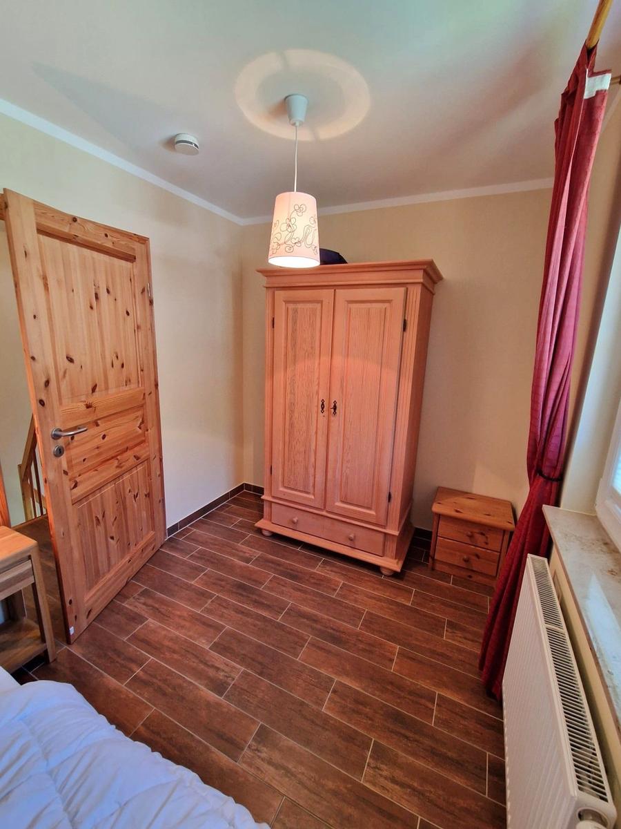 Schlafzimmer mit Holzboden, Kleiderschrank und Fenster mit Vorhang.