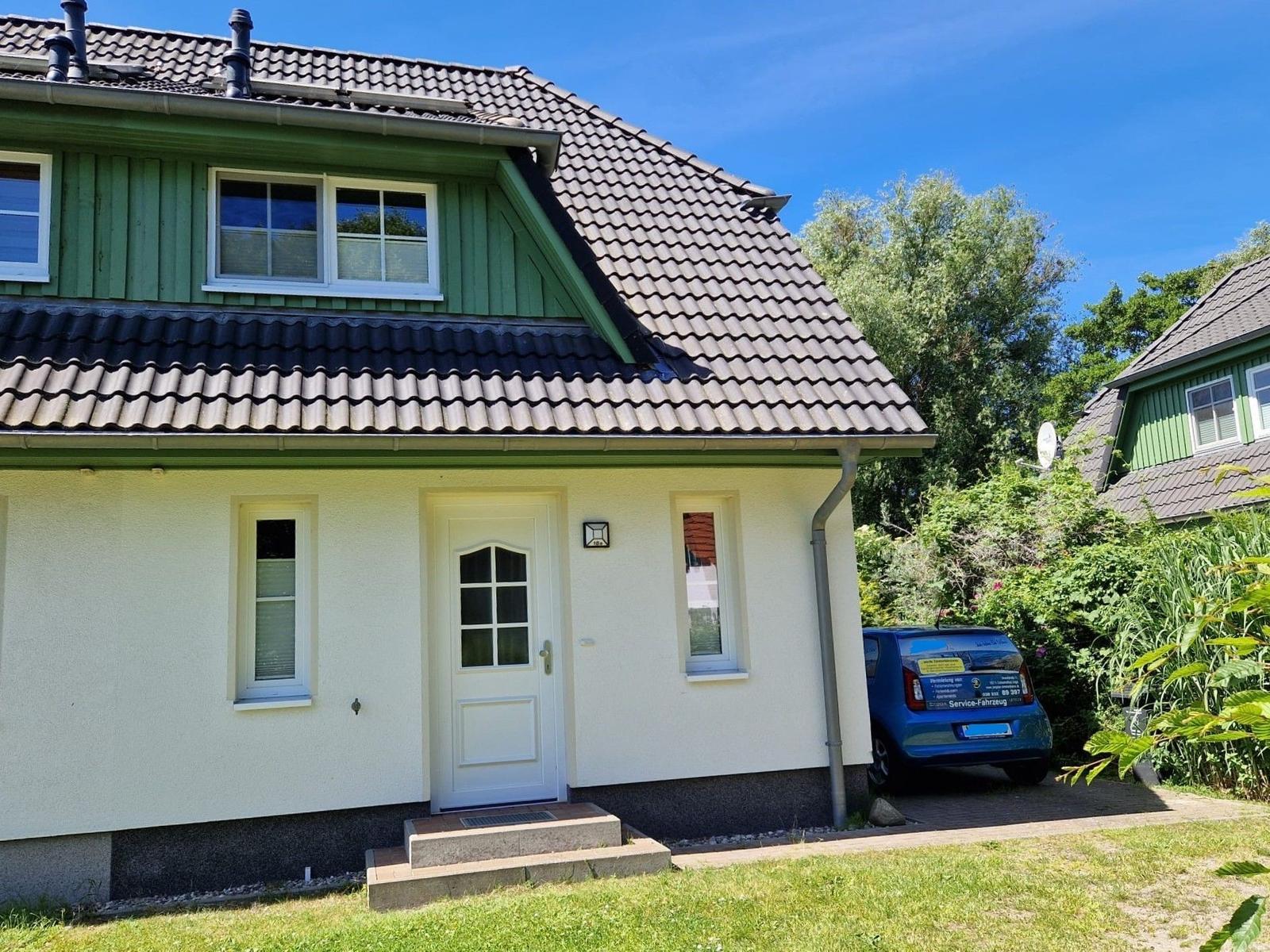 Ein Haus mit grünem Obergeschoss und weißer Fassade, Vordertür und Parkplatz.