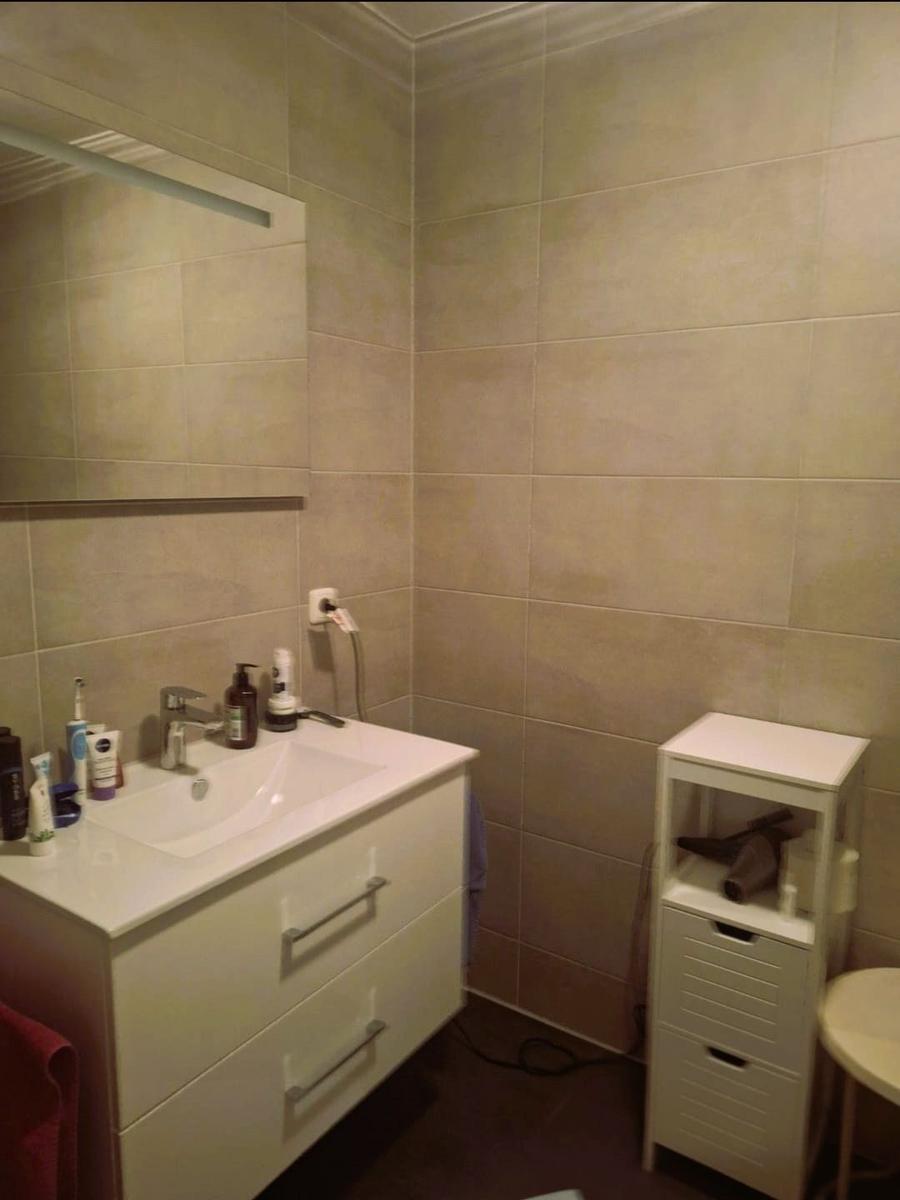 Badezimmer mit Waschbecken, Spiegel und Aufbewahrungsregal.