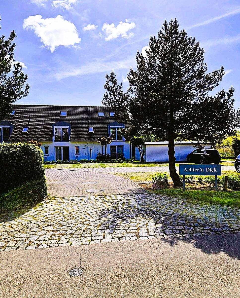 House with stone path and sign Achtern Diek under blue sky.