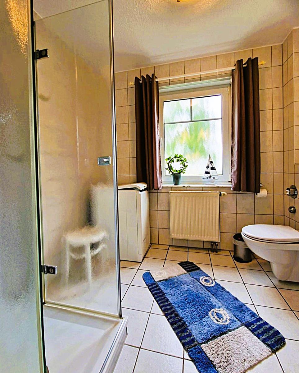 Bathroom with shower, toilet, and window with curtains.