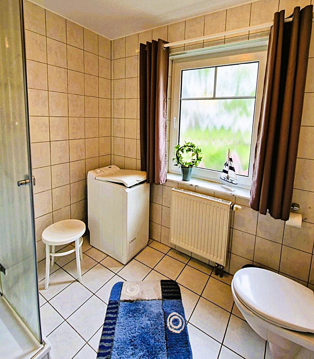 Bathroom with shower, washing machine, toilet, and window with curtains.