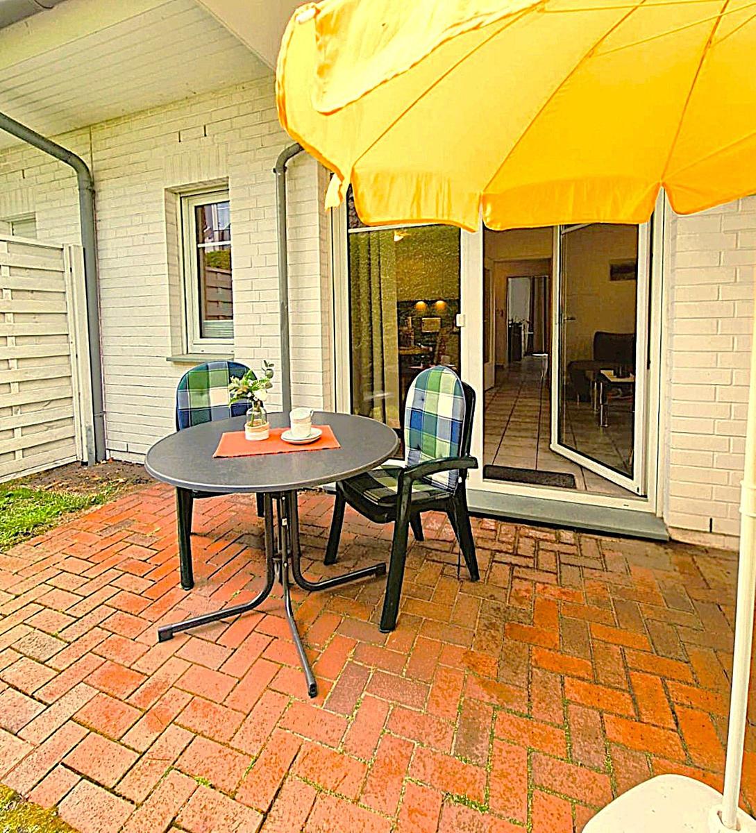 Terrace with table, two chairs, and yellow umbrella. Through glass doors, the apartment is visible.