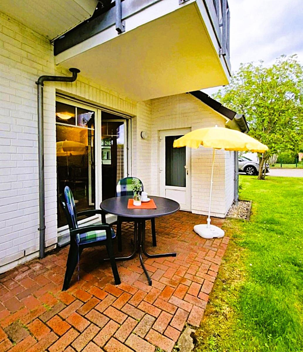 Terrace with table, two chairs, and yellow umbrella. Background: green lawn and tree.