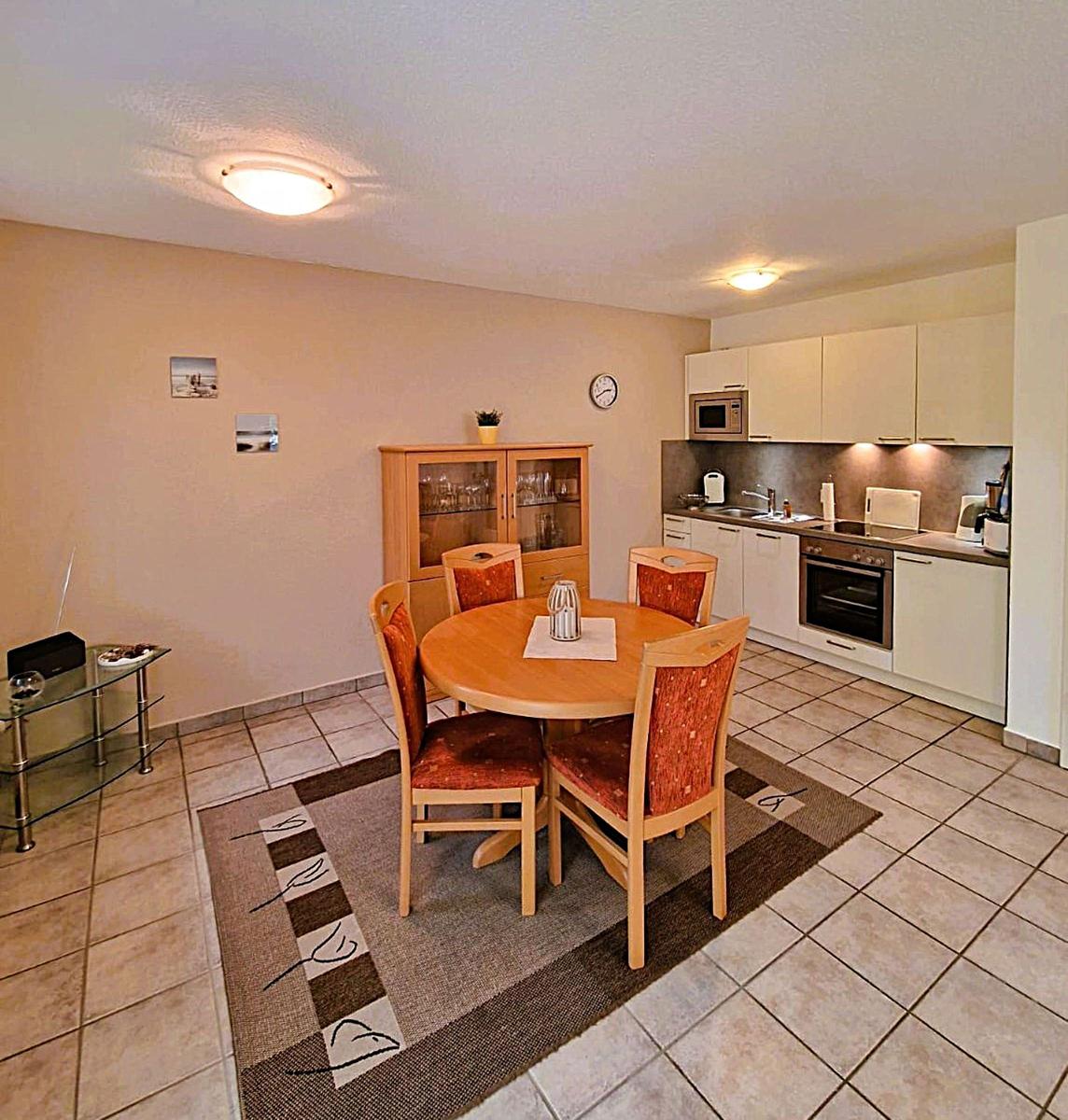 Dining room with round table, four chairs, and kitchen area with white cabinets.