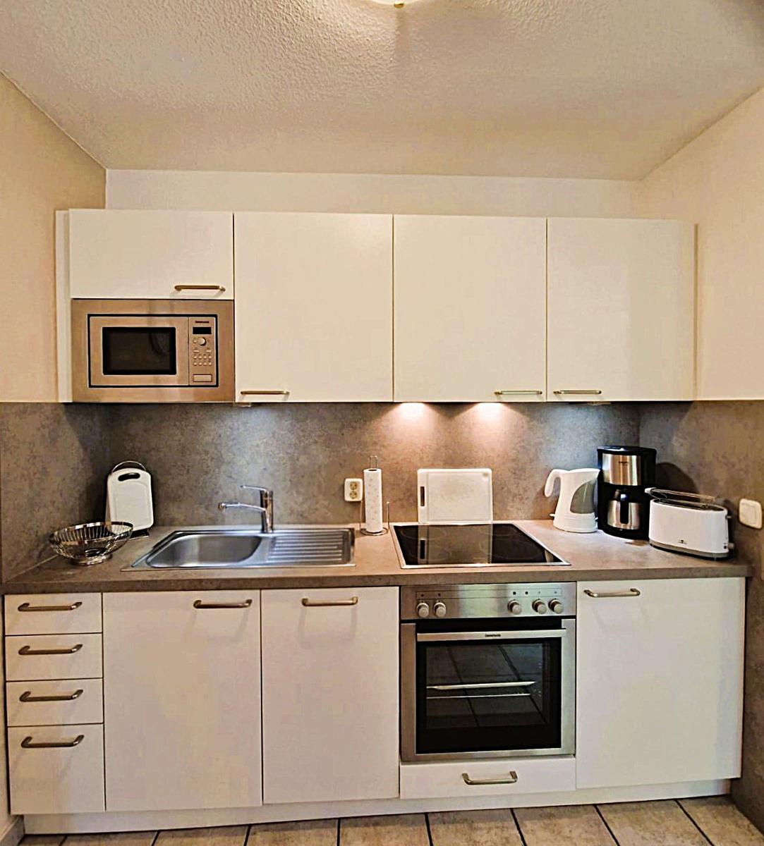 Kitchen with white cabinets, stove, sink, and microwave.