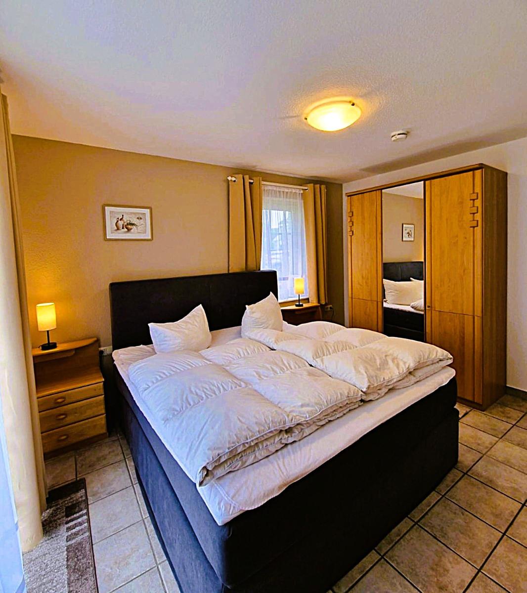Bedroom with double bed, wooden wardrobe, and nightstand with lamp.