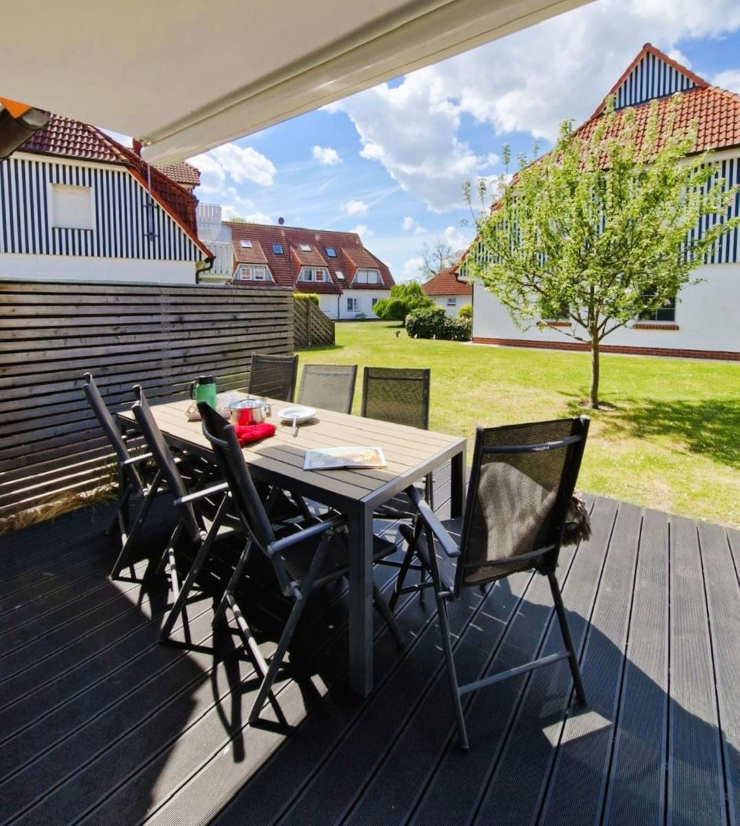 Terrasse mit Tisch und Stühlen unter Markise. Grünfläche und Häuser im Hintergrund.