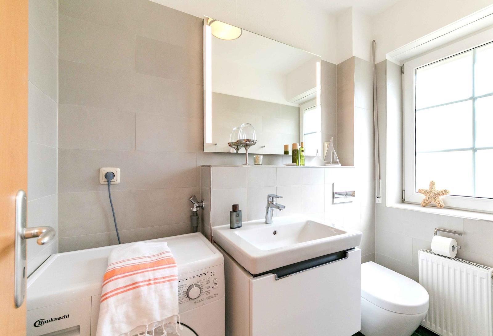 Badezimmer mit Waschmaschine, Waschbecken und Toilette. Fenster mit Sternfischdekoration.