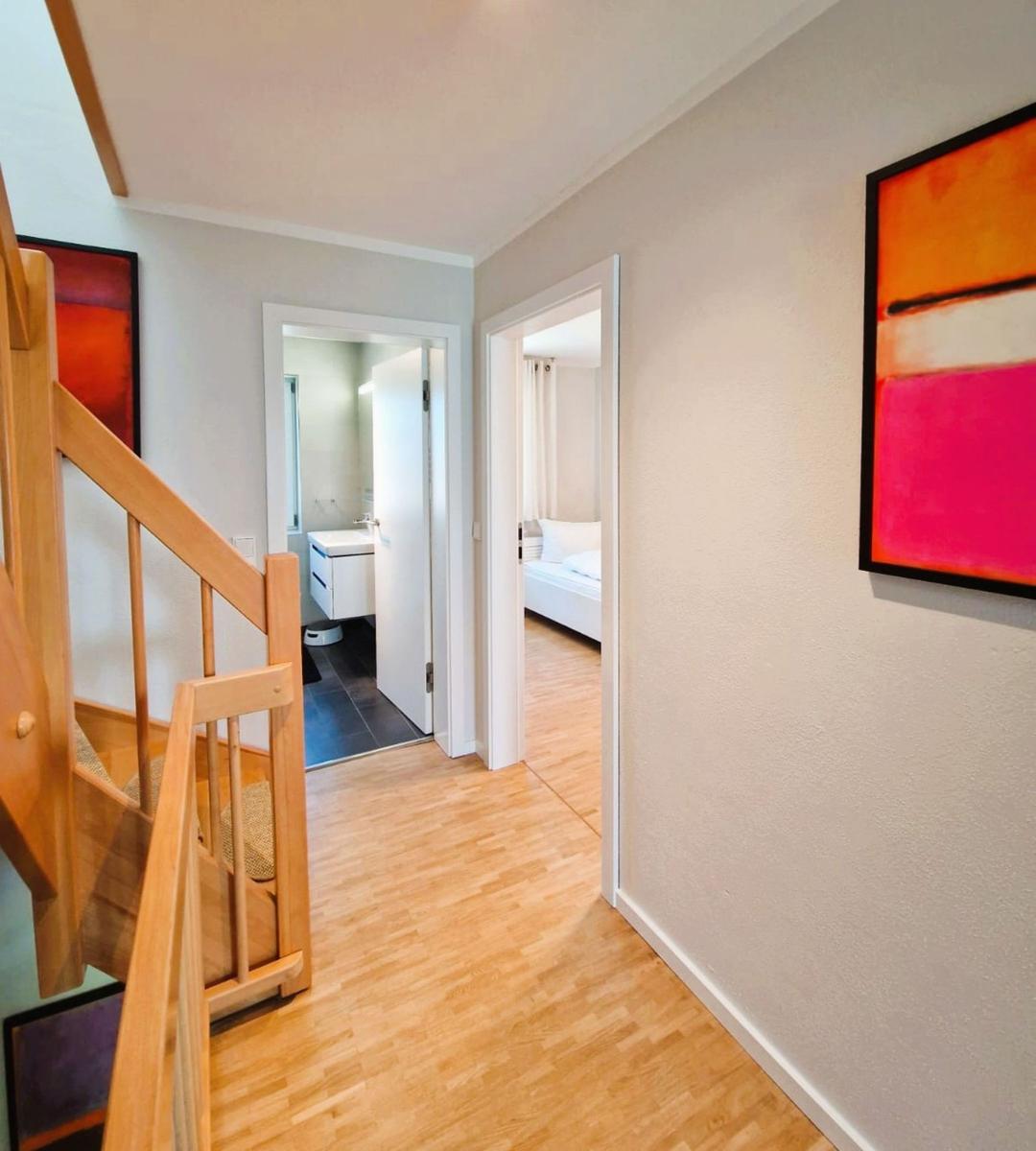 Flur mit Holztreppe, Blick in Schlafzimmer und Bad.