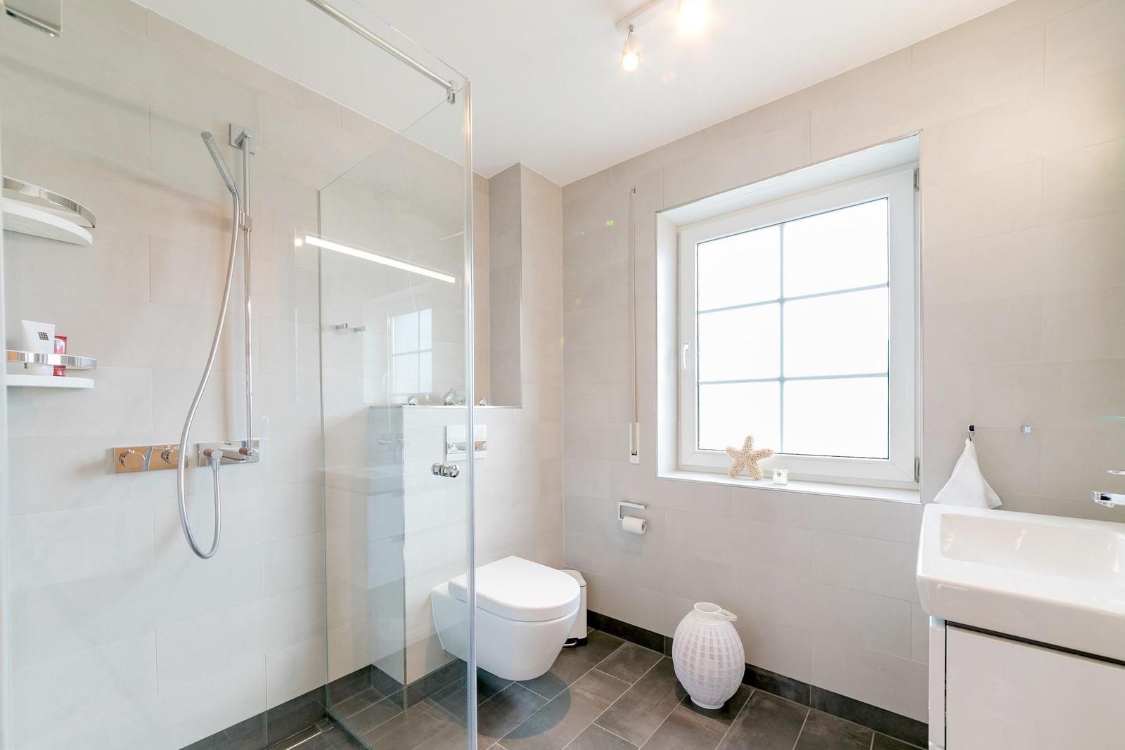 Bad mit Dusche, Toilette und Waschbecken. Fenster mit Sternfischdekoration.