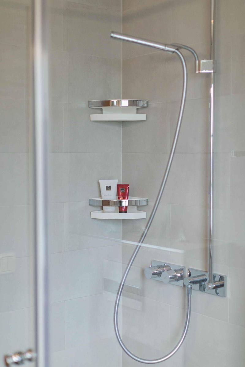 Dusche mit Duschbrause, Ablage und Seifenspender an der Wand.