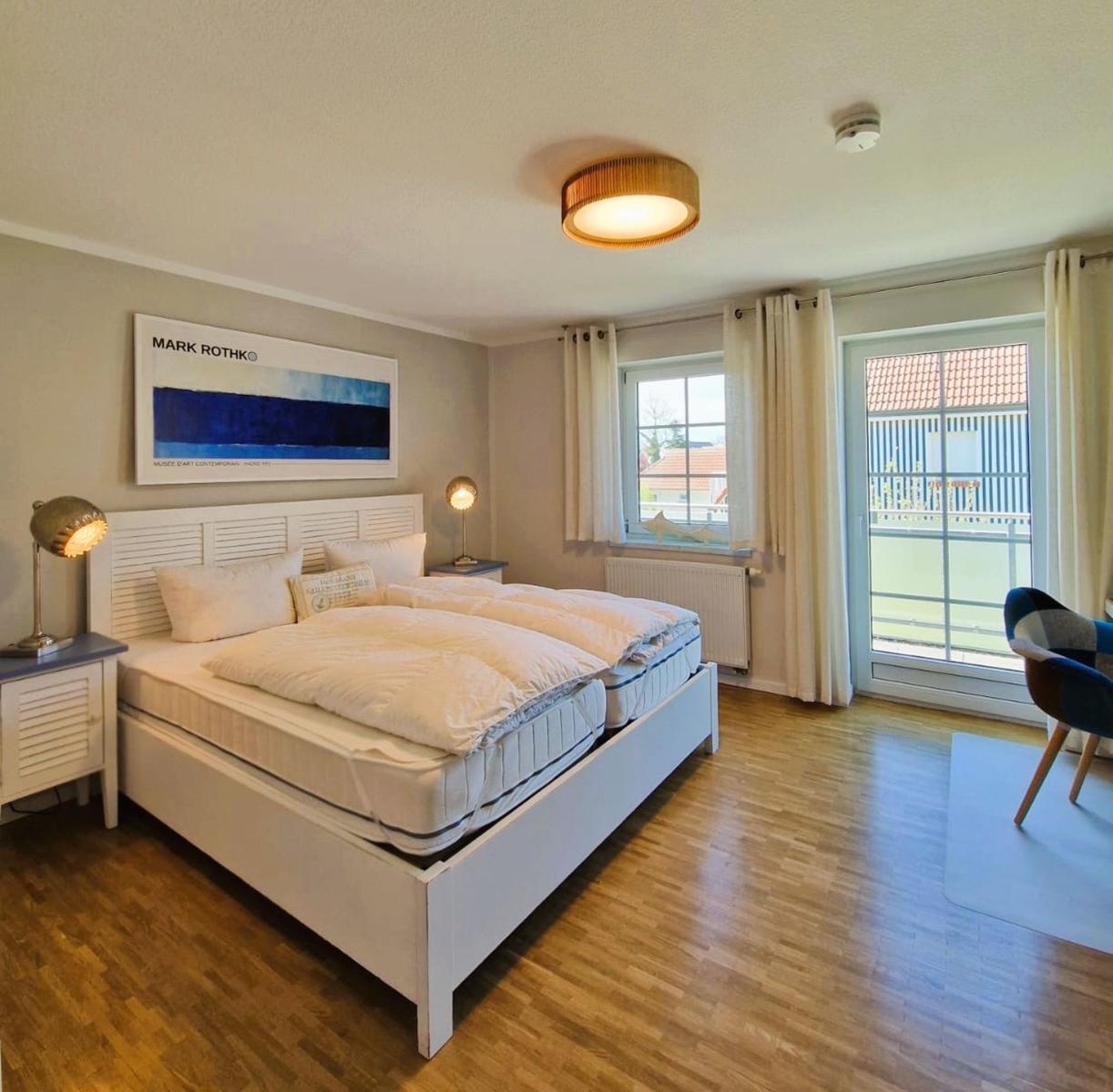 Schlafzimmer mit Doppelbett, Holzboden und Balkontür. Wandbild und Nachttische.