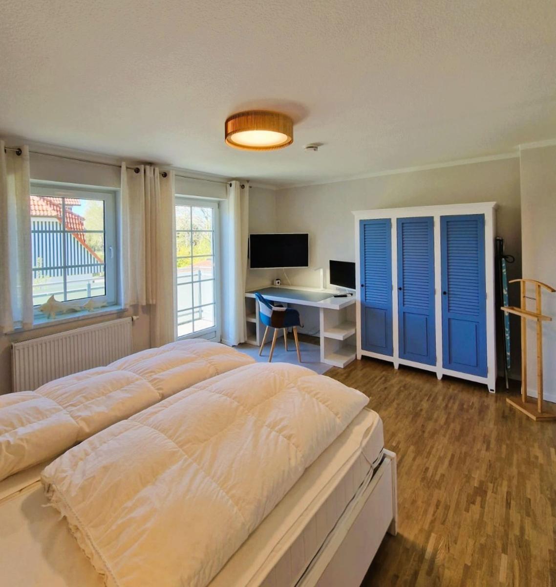 Schlafzimmer mit Doppelbett, Schreibtisch, TV und blauem Schrank.