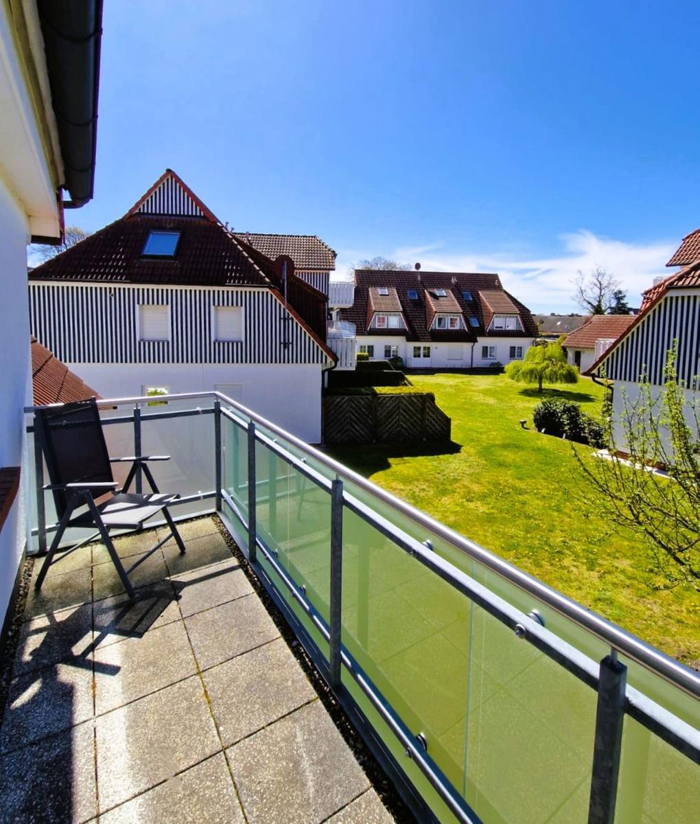 Terrasse mit Stuhl und Glasgeländer, Blick auf grünen Garten und Häuser mit Dächern.