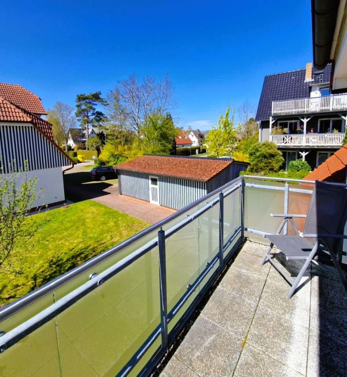 Terrasse mit Liegestuhl und Glasgeländer. Blick auf Garten und Nachbarhäuser.