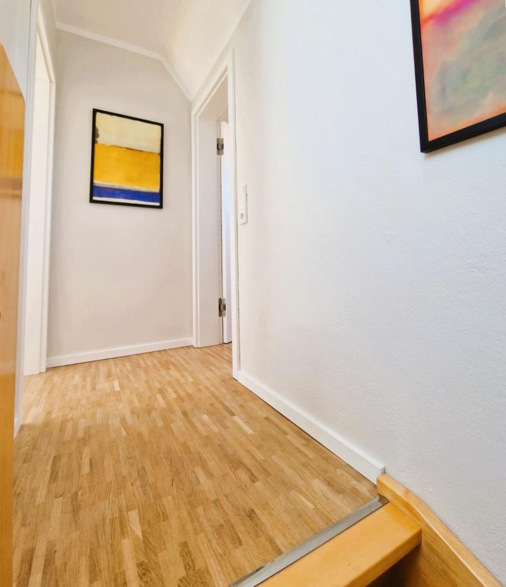 Flur mit Holzboden, weißen Wänden und zwei Bildern an der Wand.